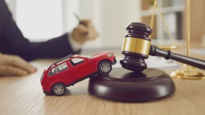 A judge with a gavel stands beside a car placed on the table.